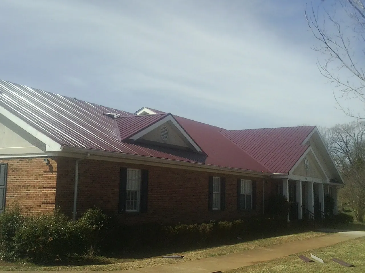 Red metal roof with gabled entries on a long brick building, from a Hail Damage Roof Repair job in Susquehanna