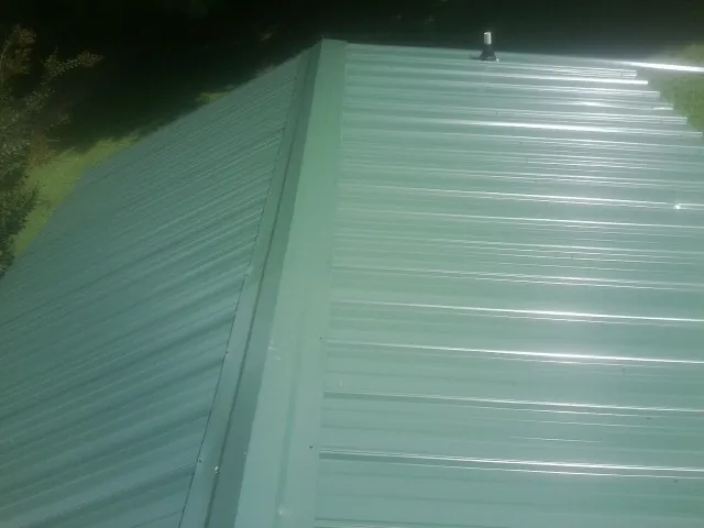 New green metal panels meeting at the ridge of a roof — Flat Roof Repair work by our crew in Susquehanna