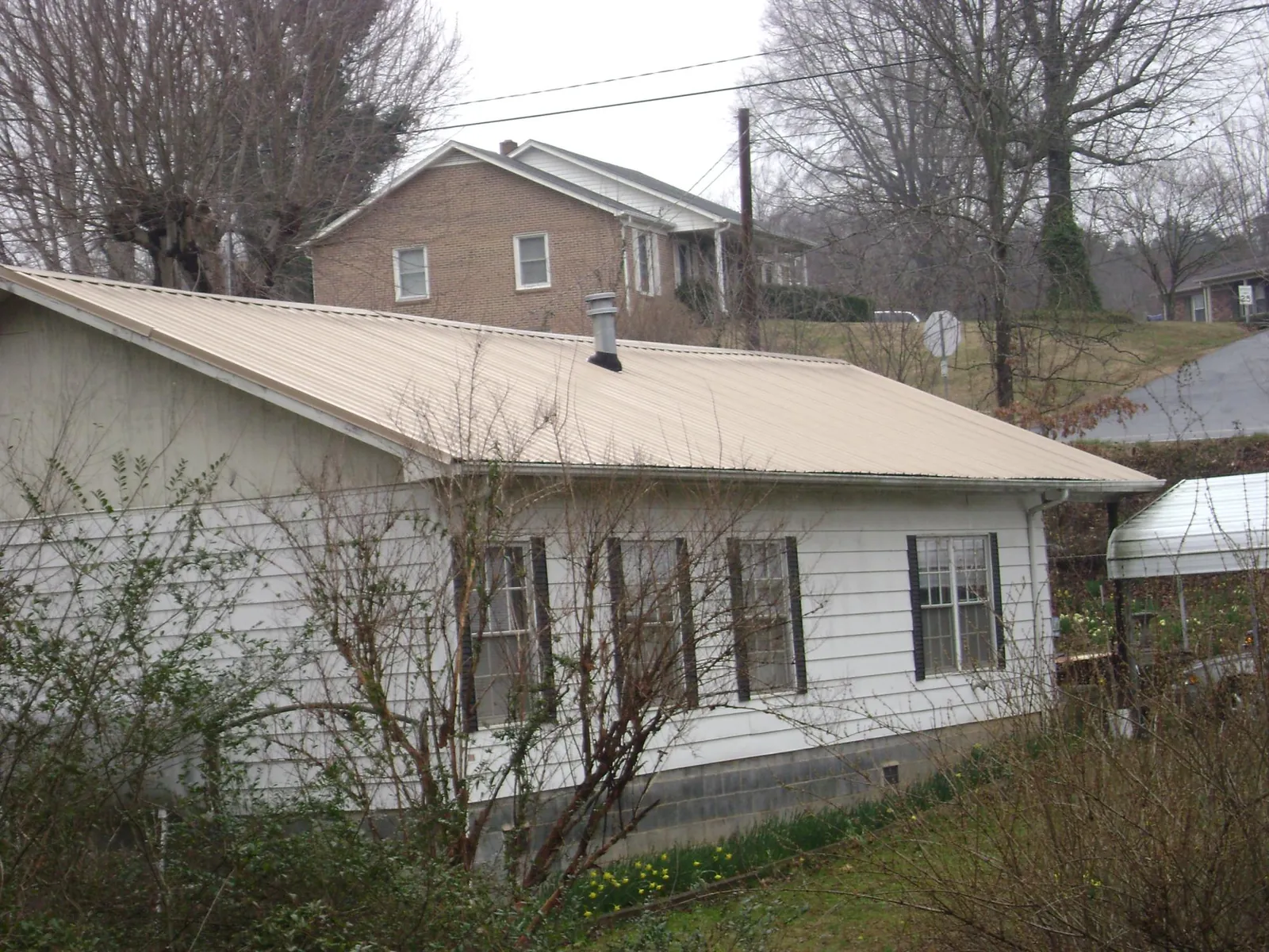 Tan metal roof on a white sided house set into a hillside — Commercial Roofing by Roofing Brothers in Susquehanna